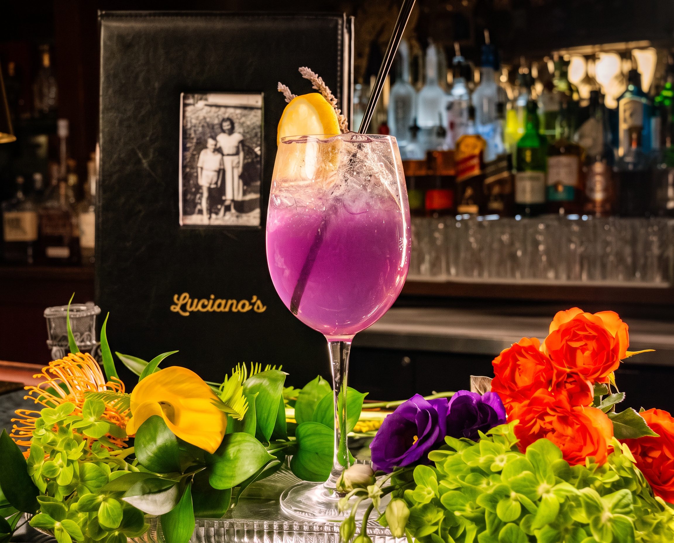 A cocktail on the bar at Luciano’s beside a bright floral arrangement