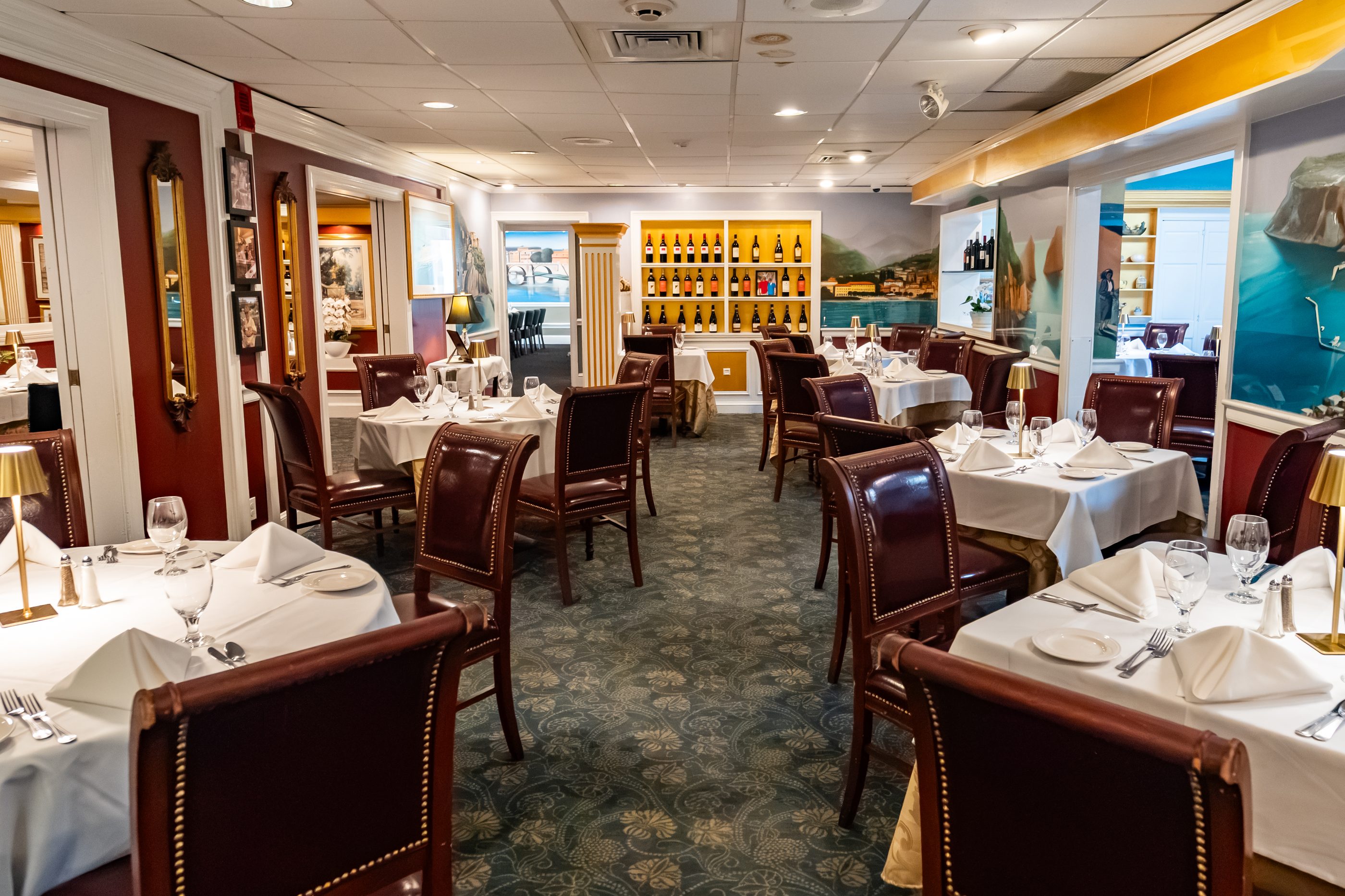 The main dining room at Luciano’s, set with white linen beneath the hand-painted coastal murals