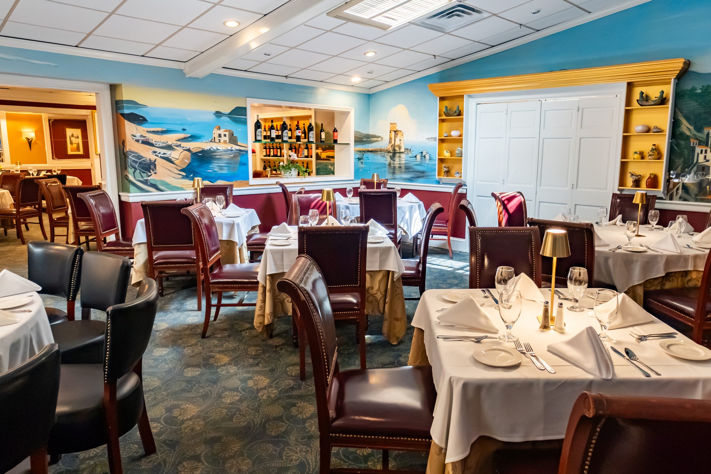 A dining room at Luciano’s lined with hand-painted Italian coastal scenes, set for dinner