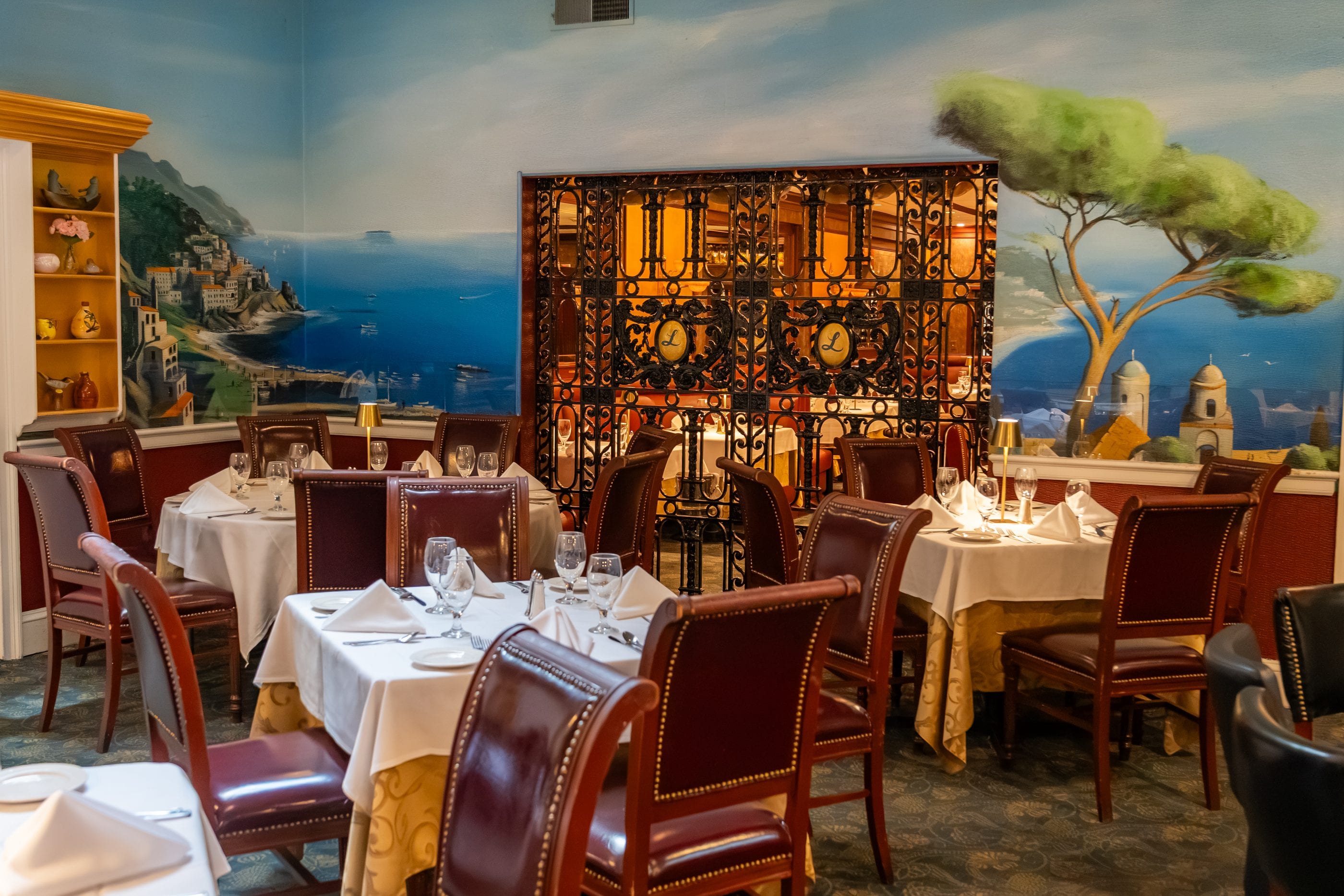 A hand-painted Mediterranean coast mural beside the wine display at Luciano’s